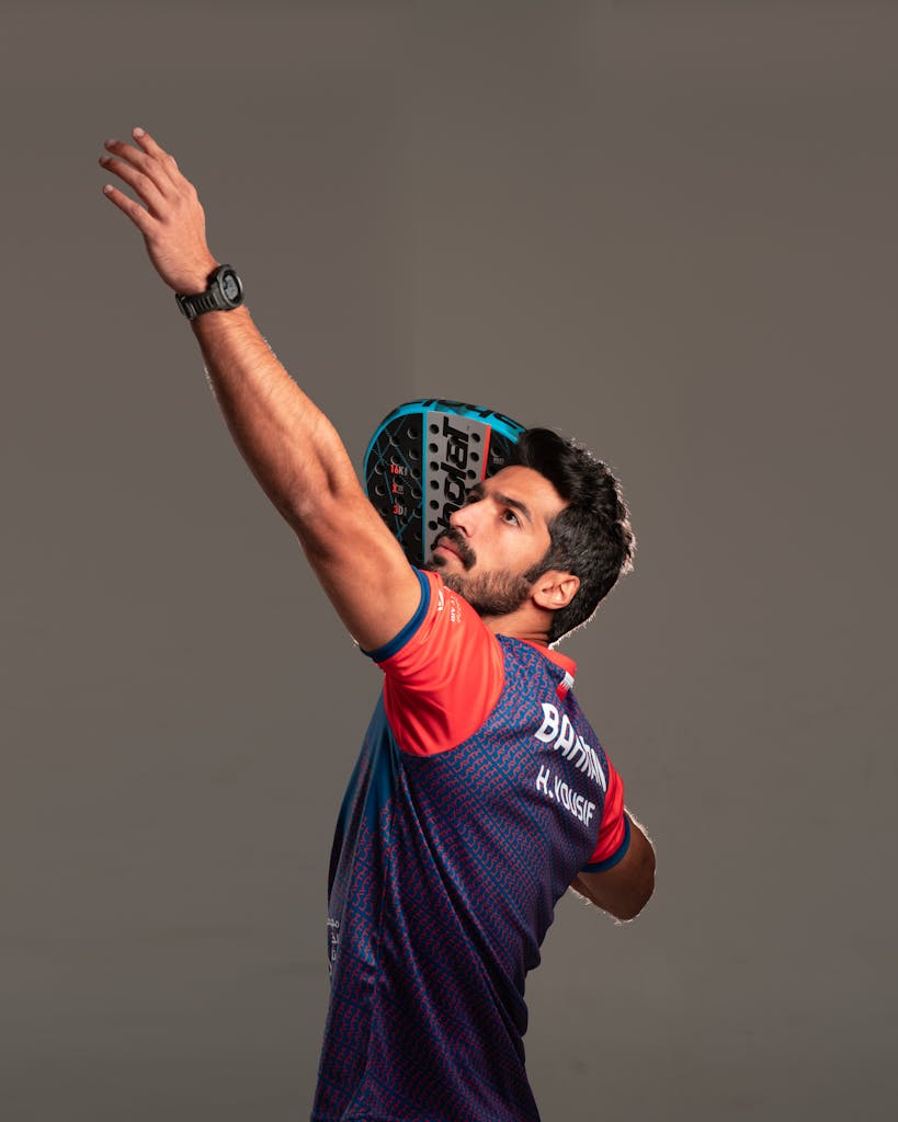 Bearded athlete in action with padel racket raised, captured in an indoor setting.