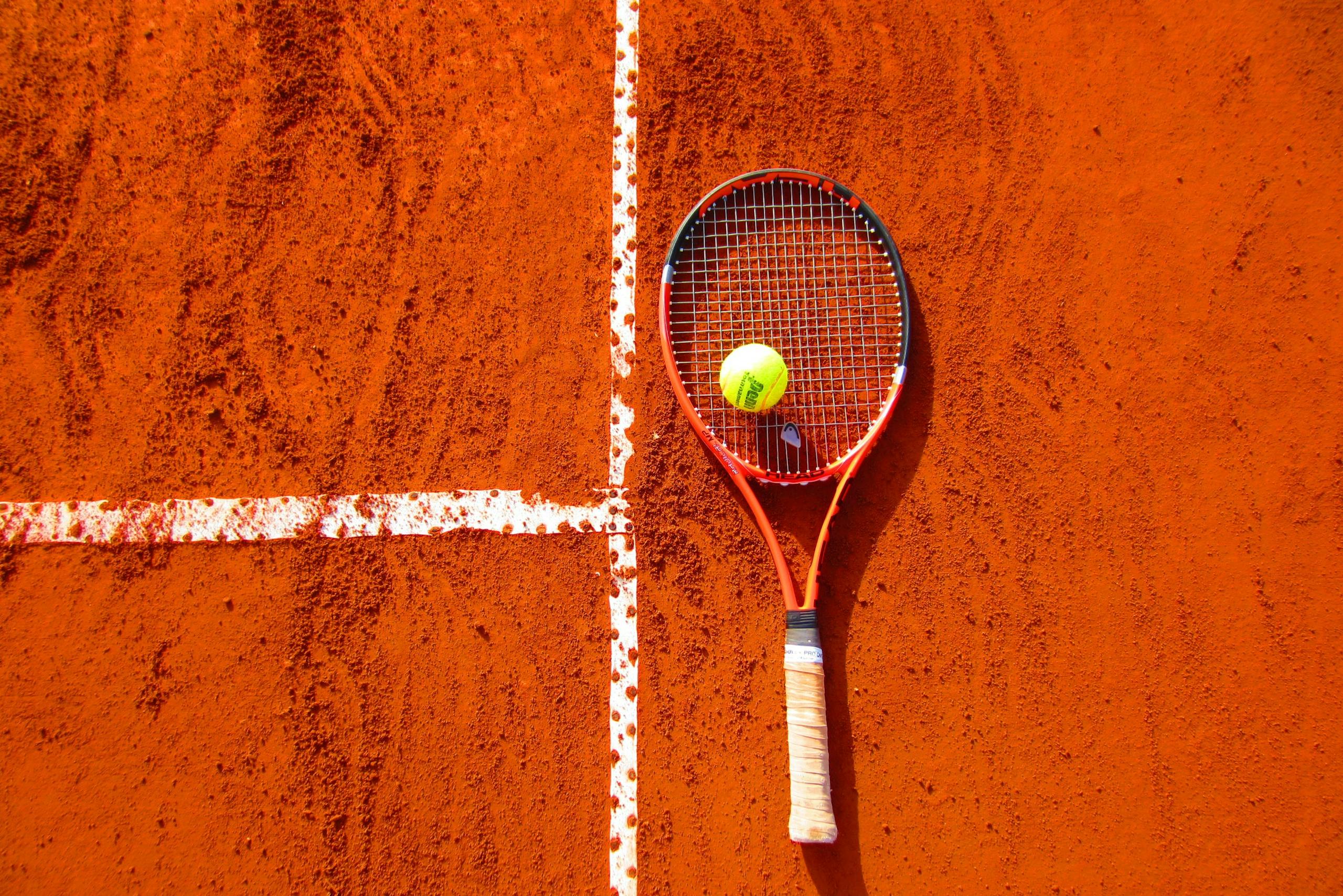 Tennis racket and ball on red clay court, ideal for sports-themed content.