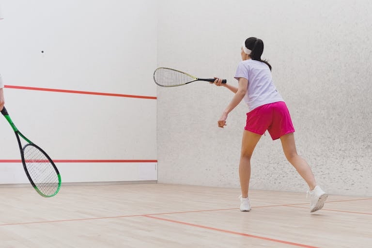 Woman playing squash on an indoor court, focused on the game with racket in hand.