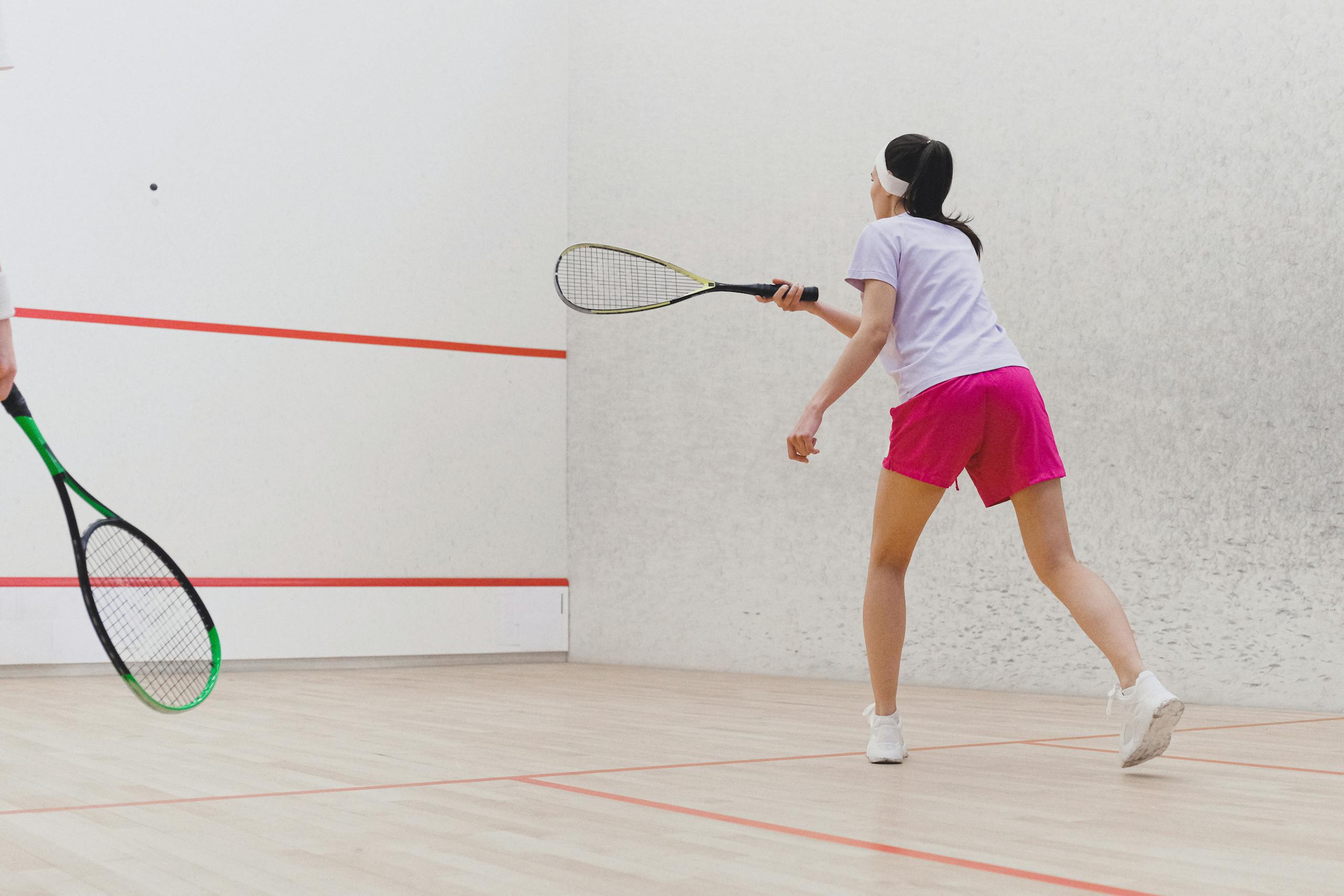 Woman playing squash on an indoor court, focused on the game with racket in hand.