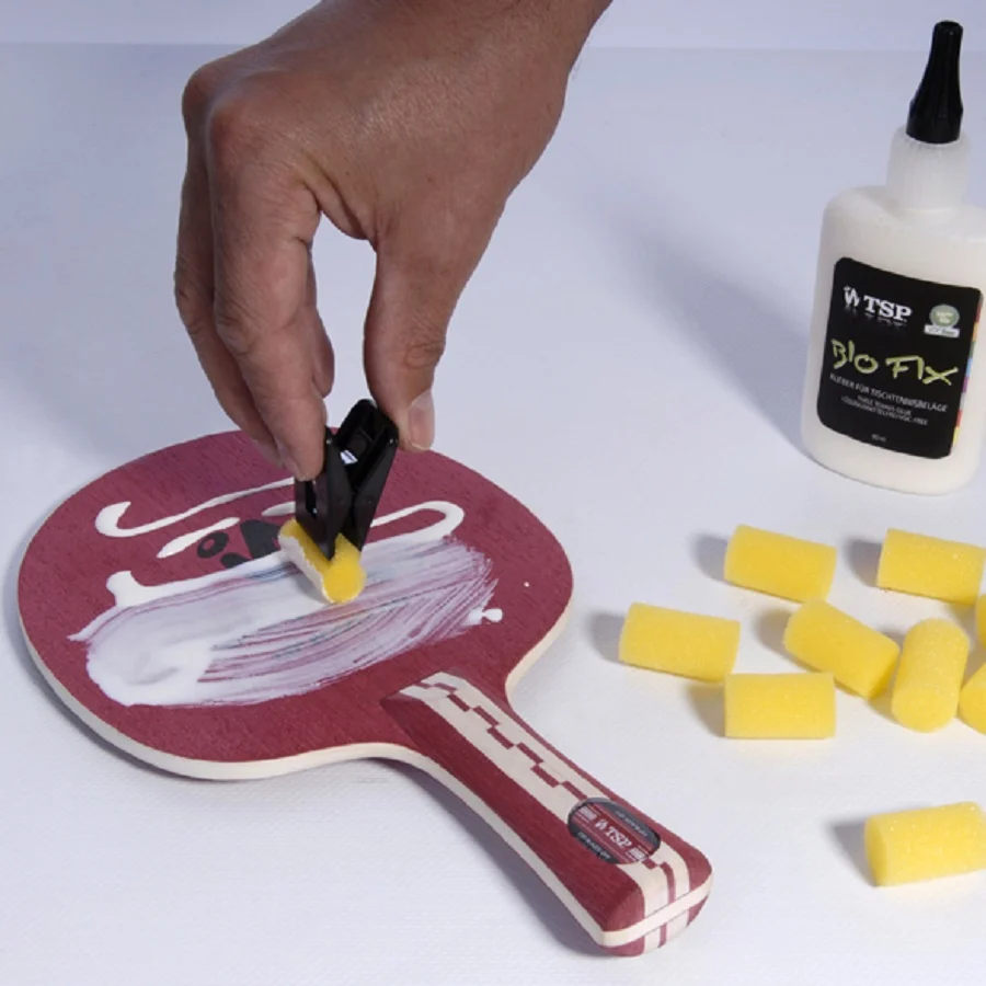Applying water-based table tennis glue to a blade with a sponge applicator before fitting a new rubber