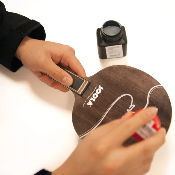 Applying a thin coat of blade sealant to a bare table tennis blade before gluing rubbers