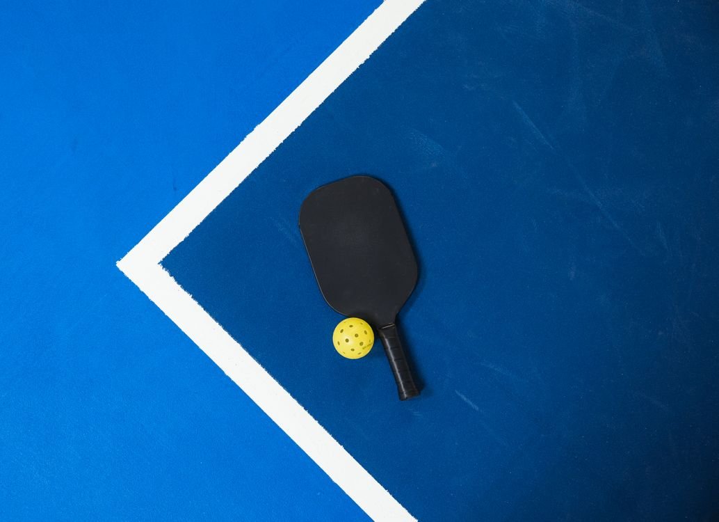 Pickleball paddle and ball resting on a blue court surface
