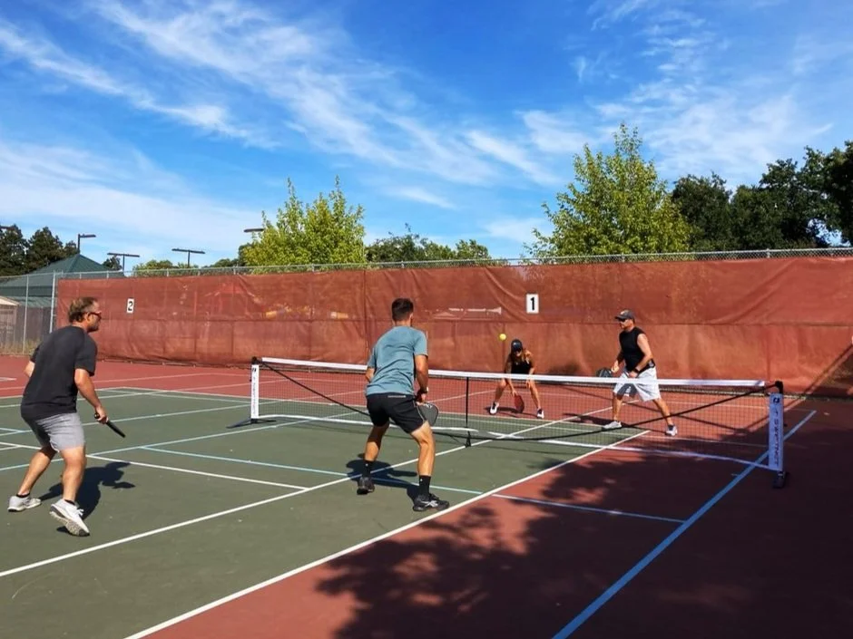 Players in a doubles game on an outdoor court with a portable pickleball net