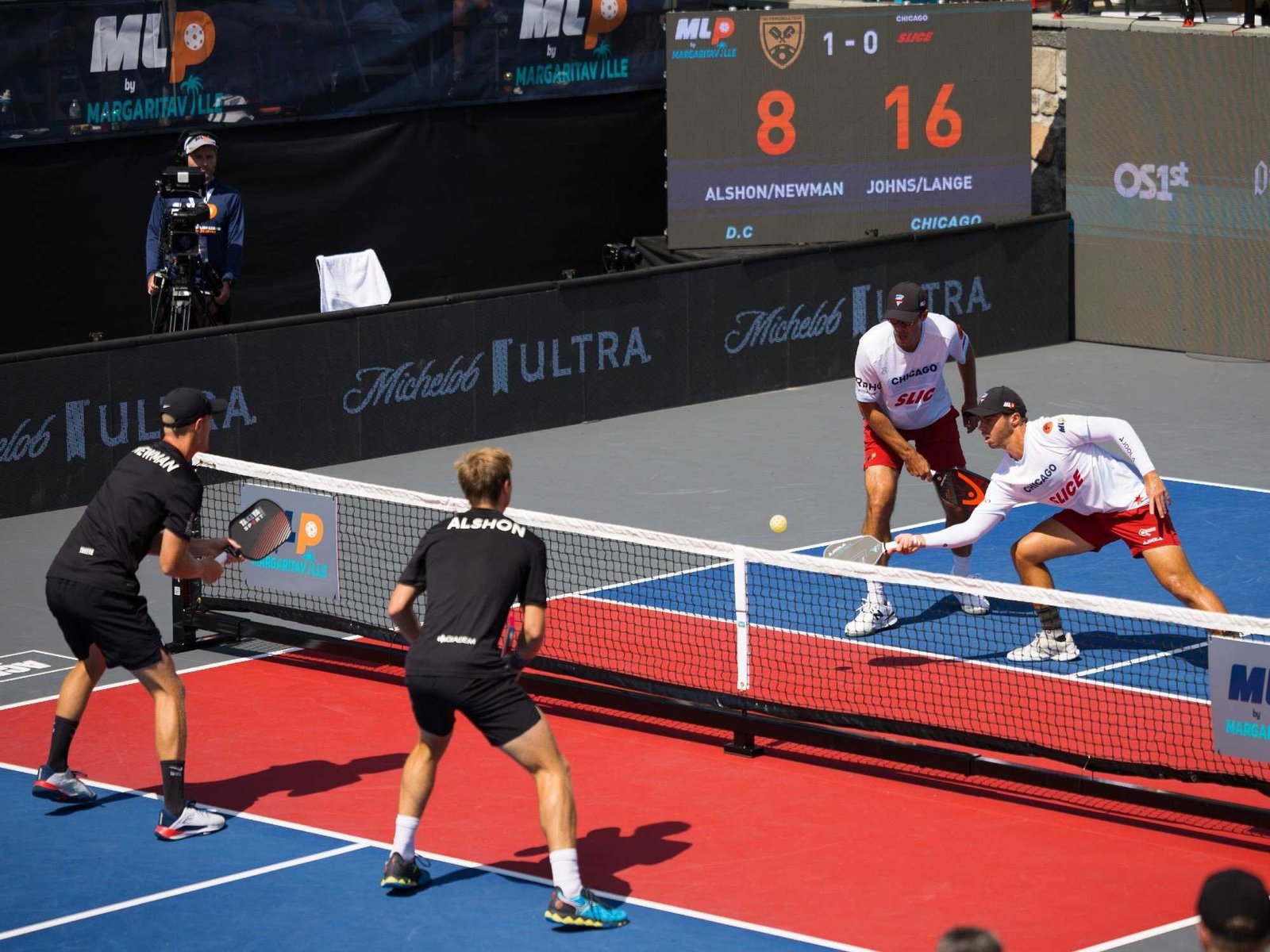 Professional pickleball doubles match with all four players positioned at the kitchen line during a fast rally