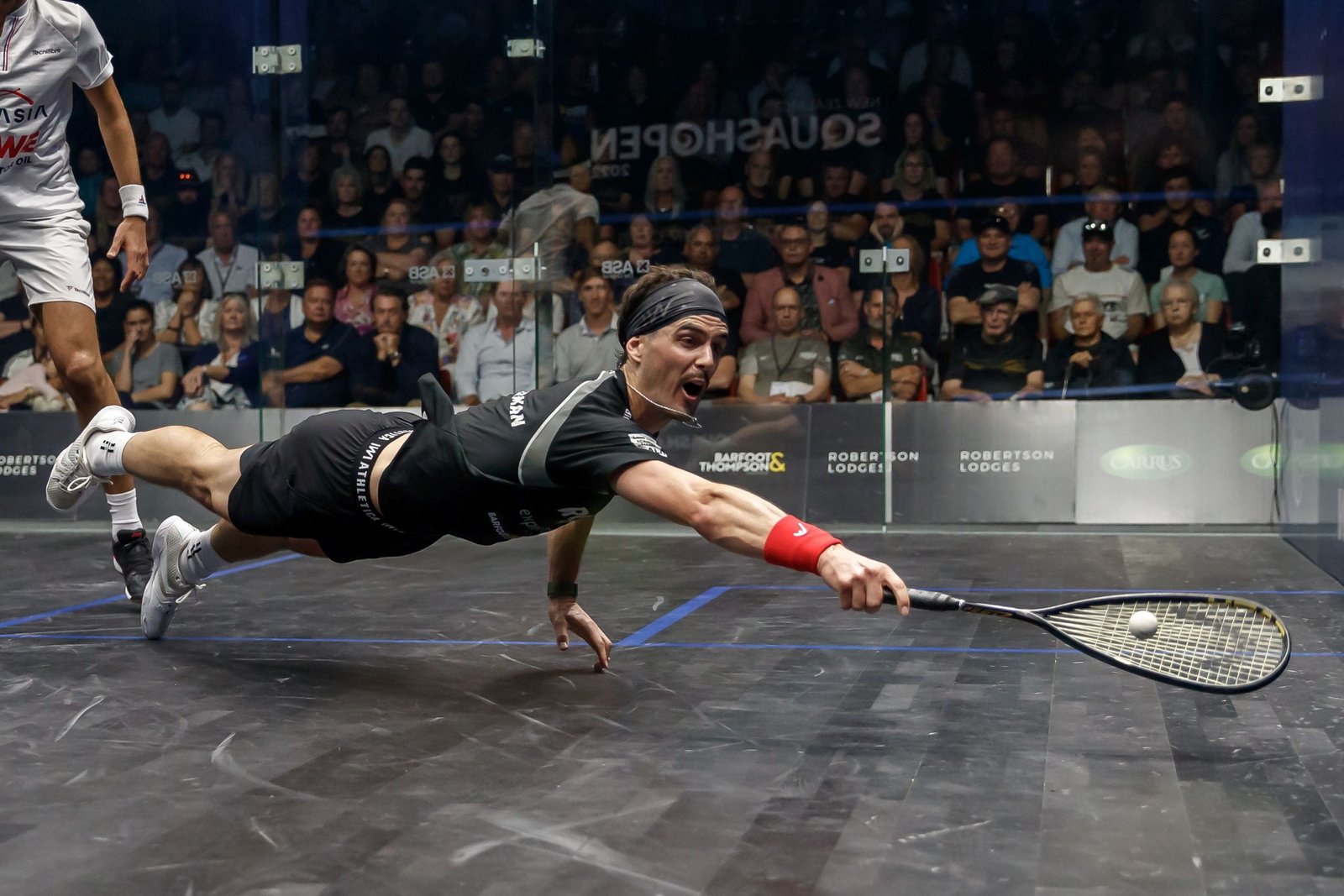 Two squash players contesting a rally deep in the back corner of a glass court