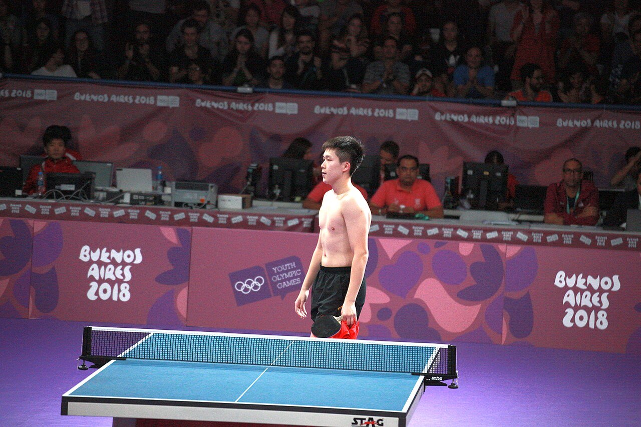 Table tennis player lunging wide to play a forehand during a competitive match