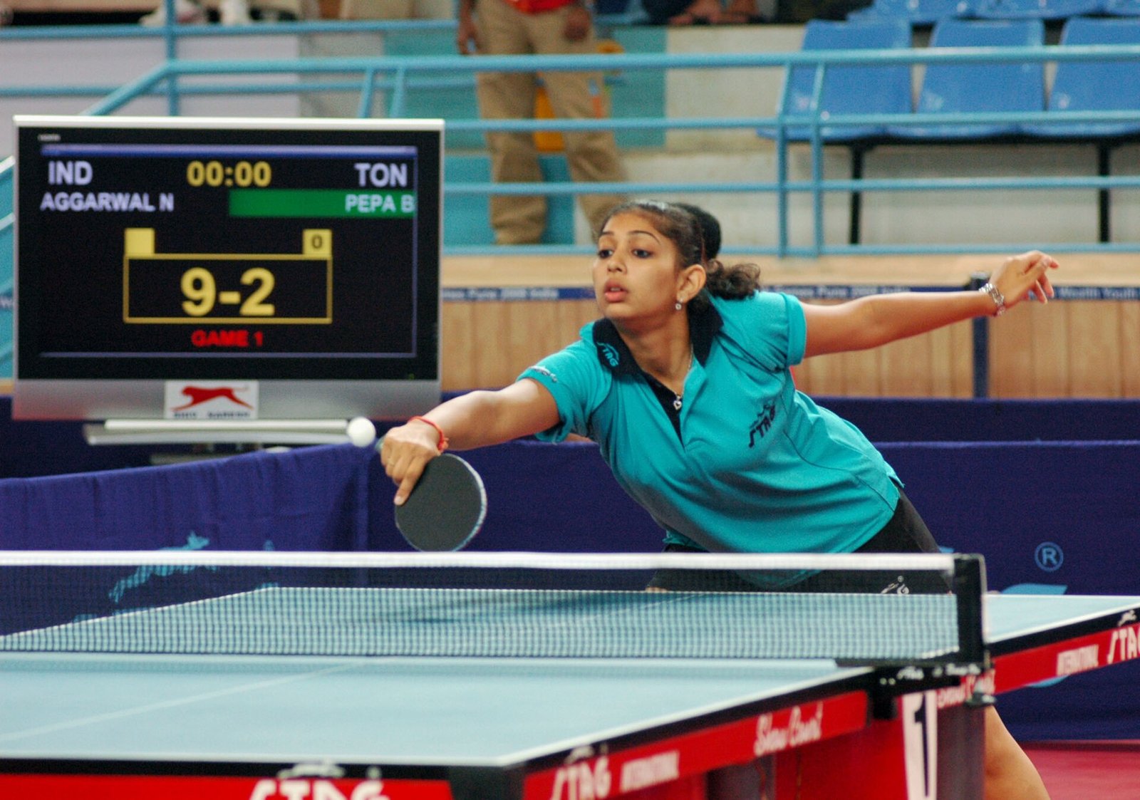 Table tennis player reaching for a wide ball during a competitive match rally