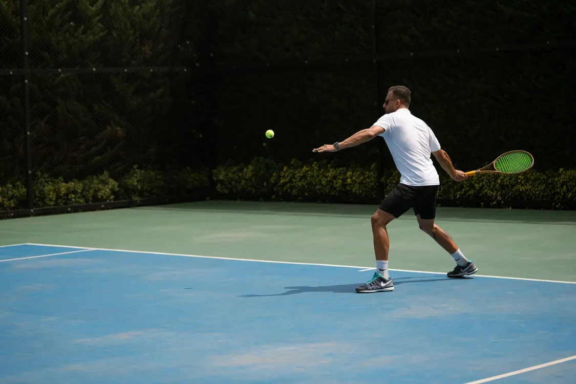 Tennis player hitting a groundstroke on an outdoor court in bright sunshine