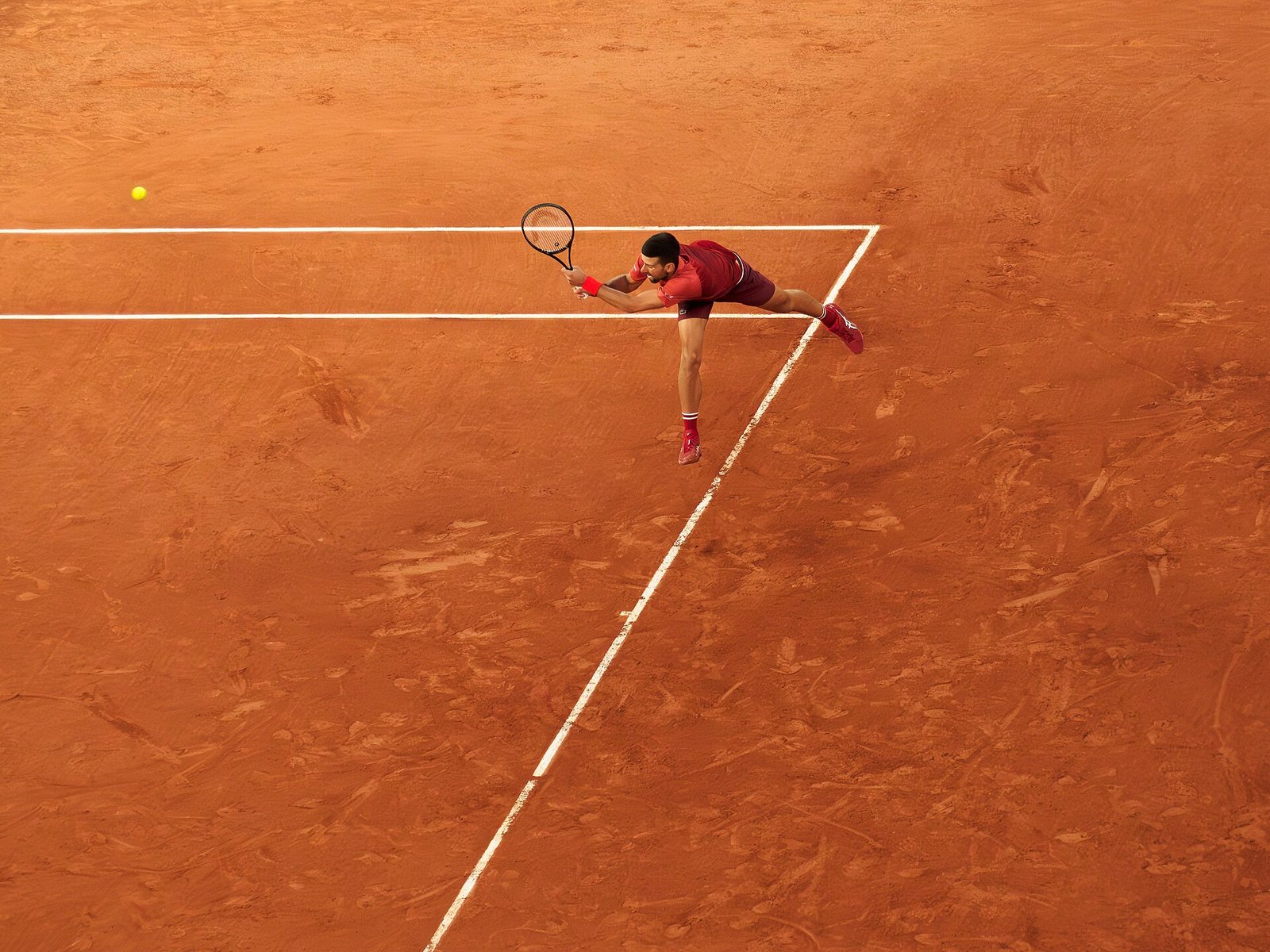 Professional tennis player stretched at full length on a clay court at Roland Garros