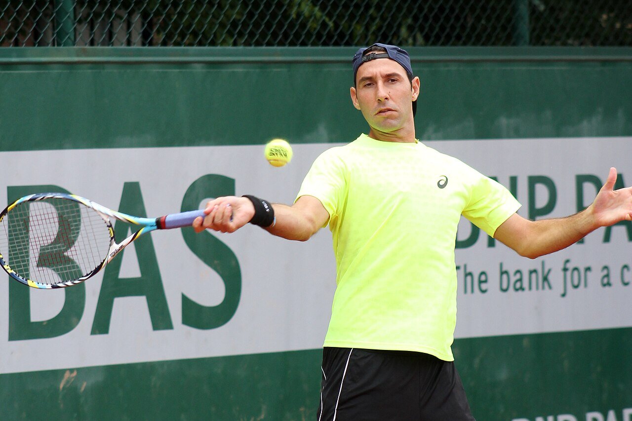 A player driving a forehand on a clay court, feet planted wide in court shoes built for lateral movement