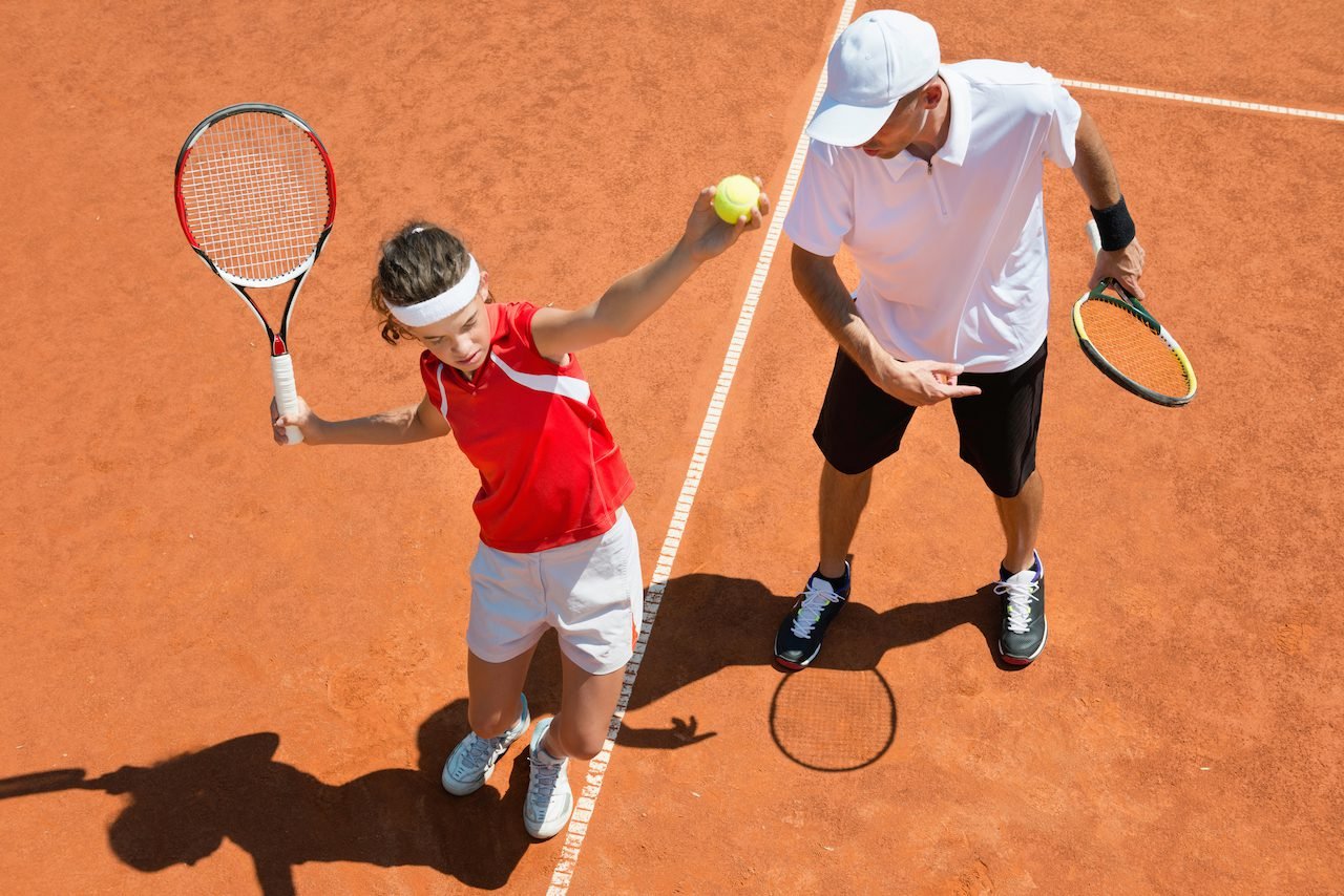 Tennis player tossing the ball to serve during a lesson on an outdoor court