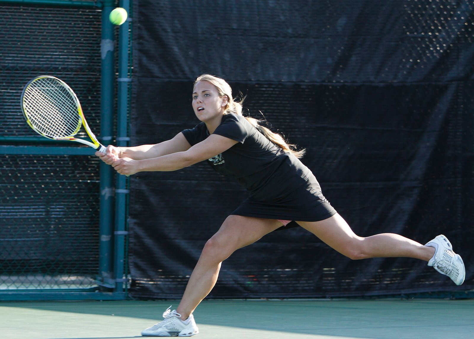 Senior-division tennis player completing a full groundstroke swing on an outdoor hard court