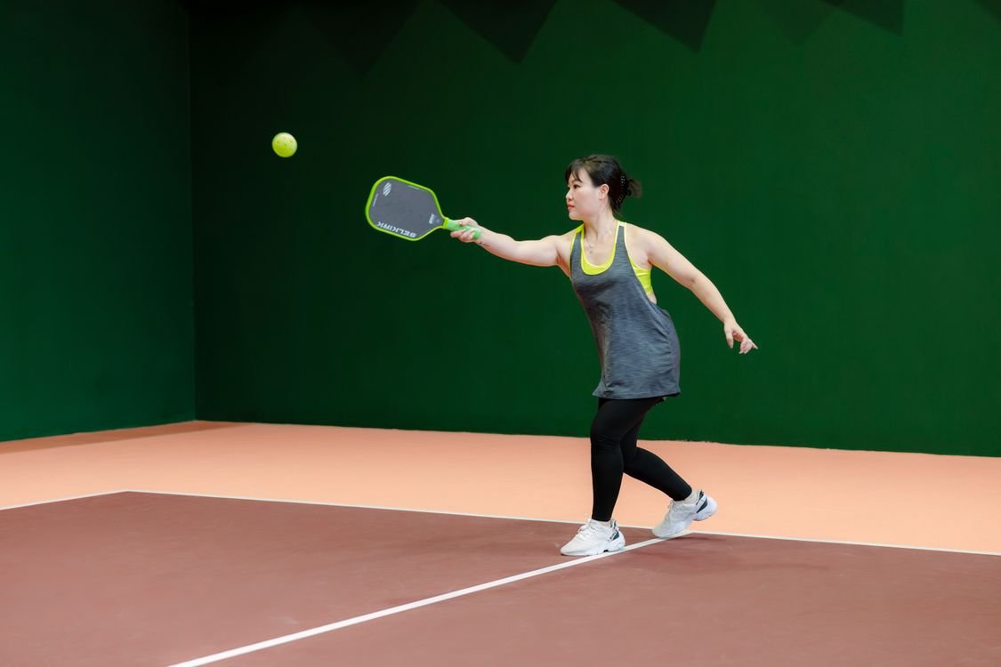 Woman playing pickleball on an indoor court, paddle in hand mid-rally