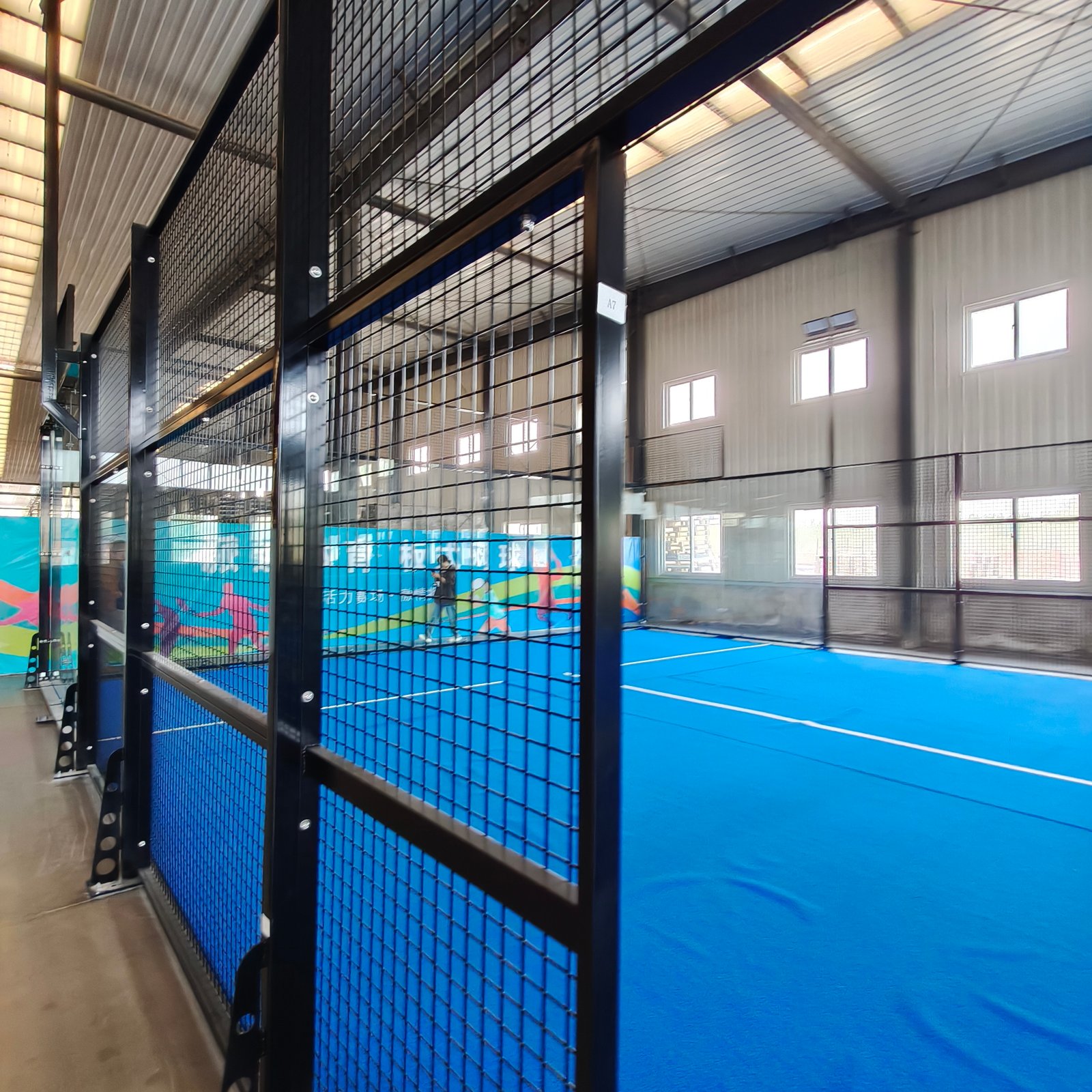 Indoor padel court installed inside a warehouse-style building, with steel mesh and glass walls under a pitched roof