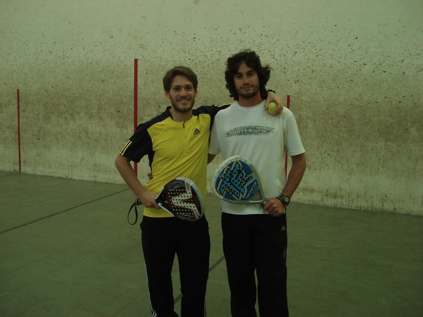 Two padel doubles partners standing side by side on court holding their rackets and smiling, ready for a social game