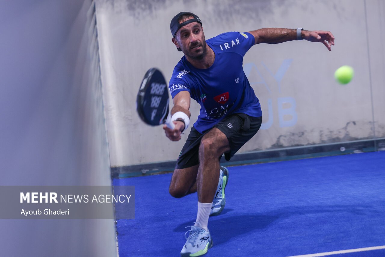 A padel player stretched low and wide to play a forehand drive across the blue court during a training session