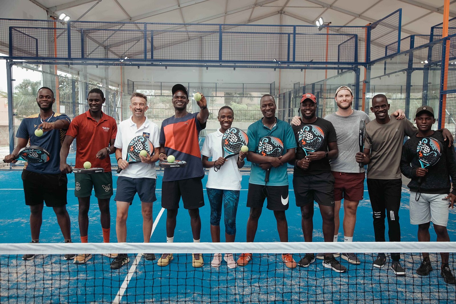 Group of padel players holding rackets and balls at the net on a covered padel court