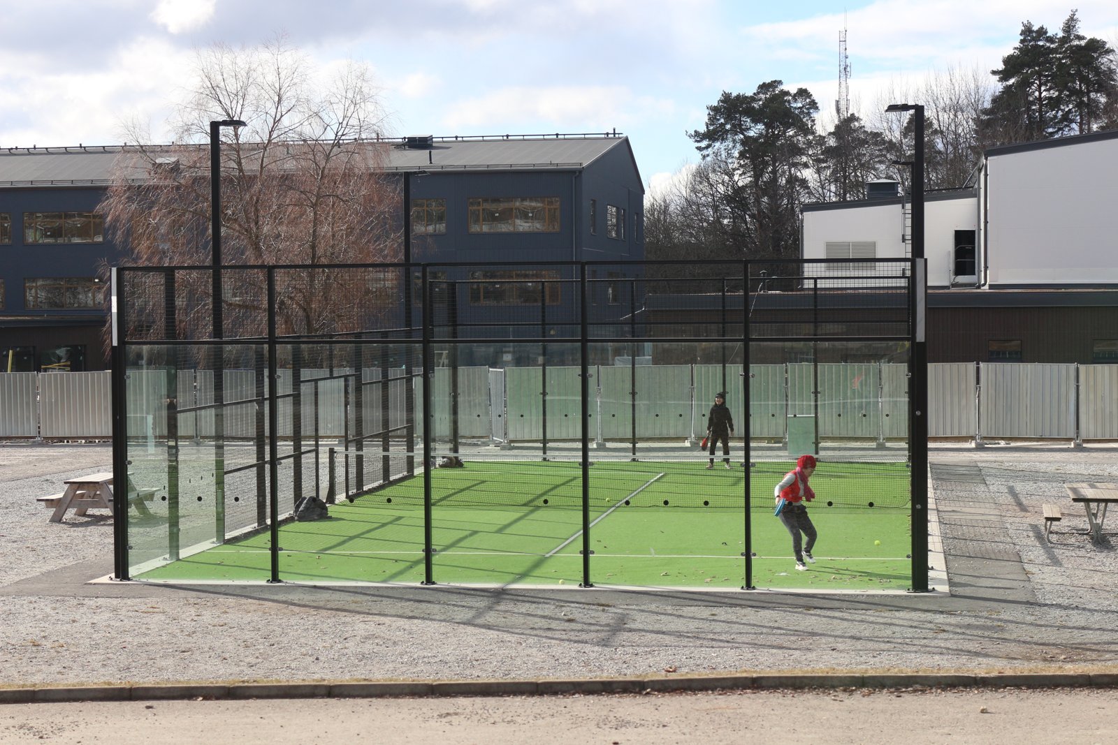 A wide view of an outdoor padel court with two players knocking up on the green surface before a game