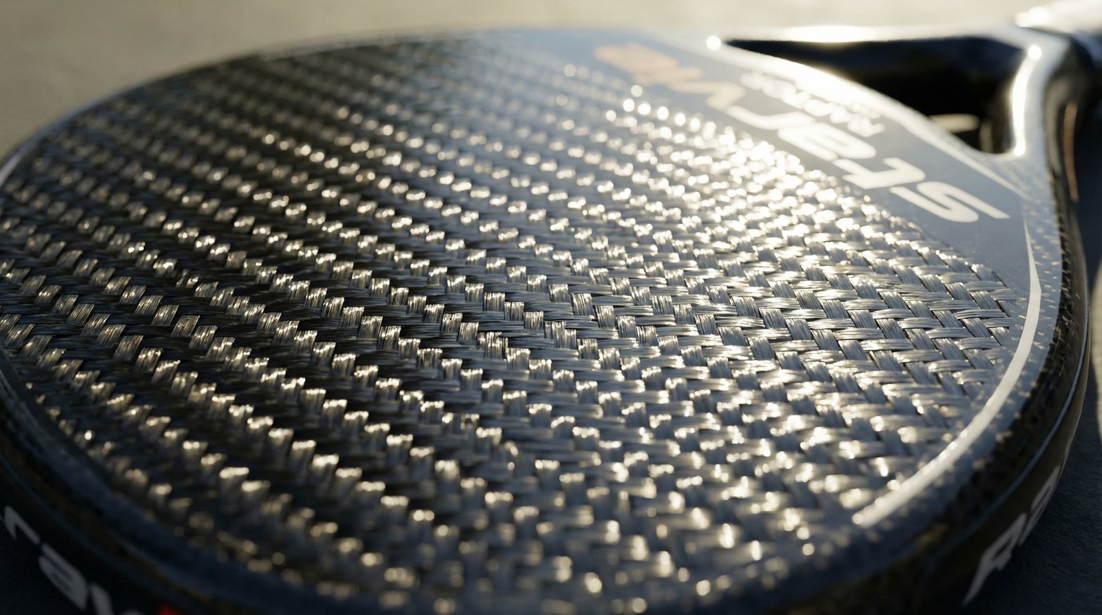 Close-up of woven carbon fibre on a padel racket face — face materials are where much of a racket's weight and stiffness live