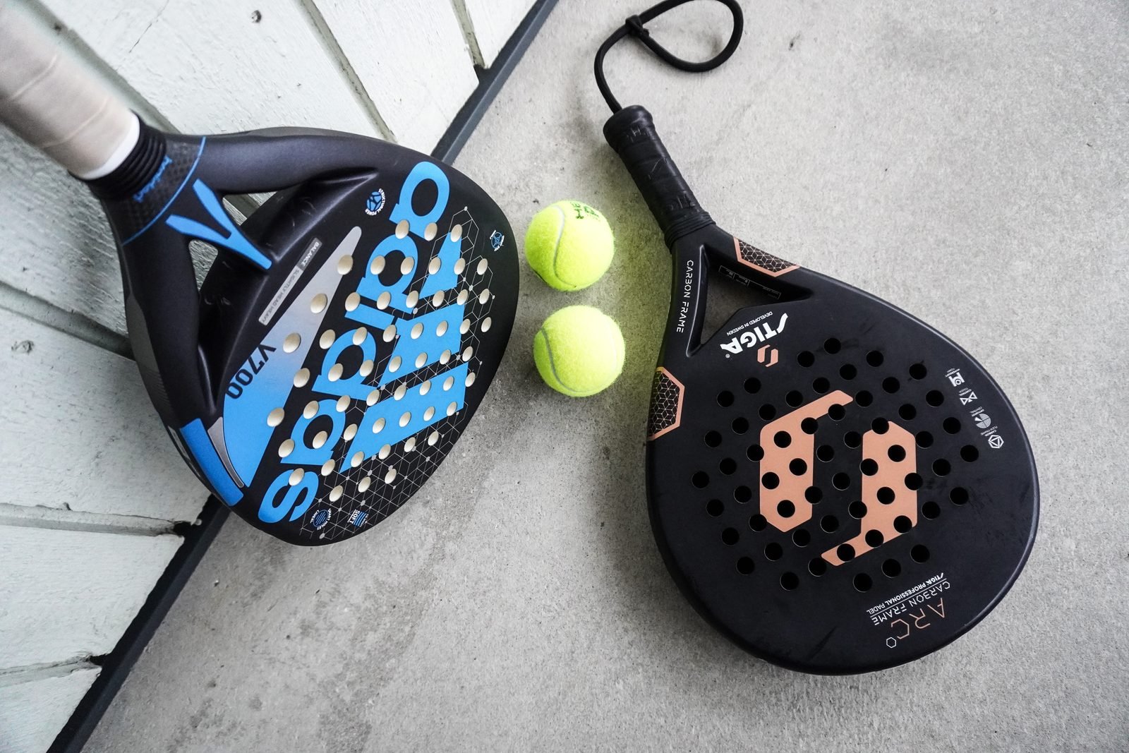 Two padel rackets and a tube of padel balls resting on a court surface