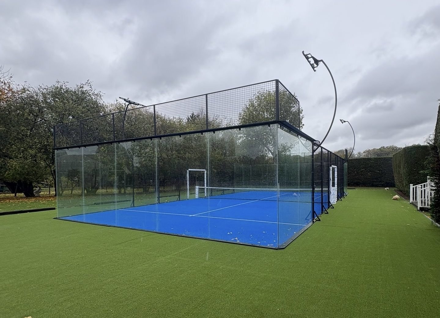 Full panoramic padel court with glass back walls and no corner pillars, photographed in daylight