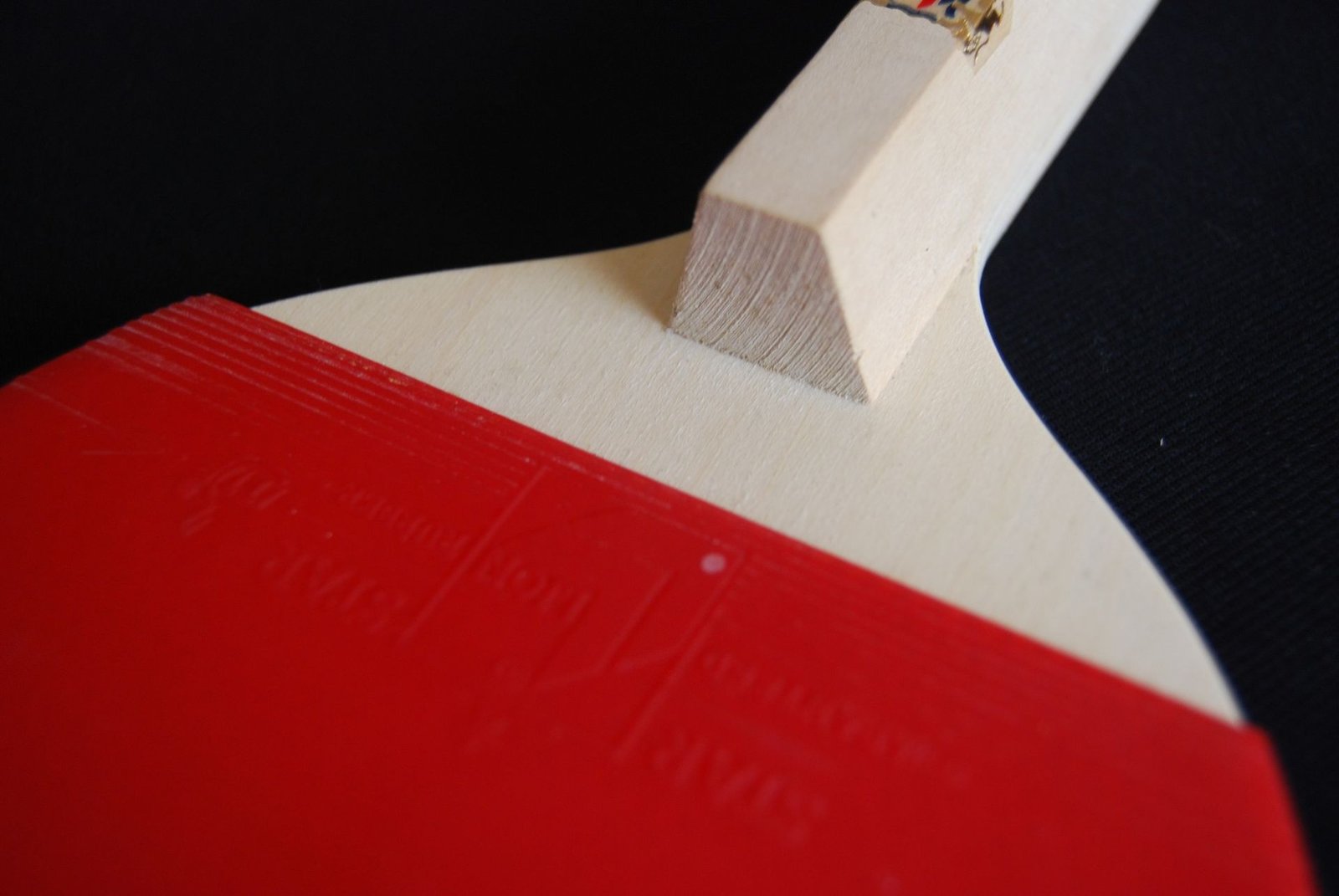Close-up of a Japanese penhold table tennis bat showing the squared cork block handle above the red rubber, shaped for the thumb and index finger to hook against