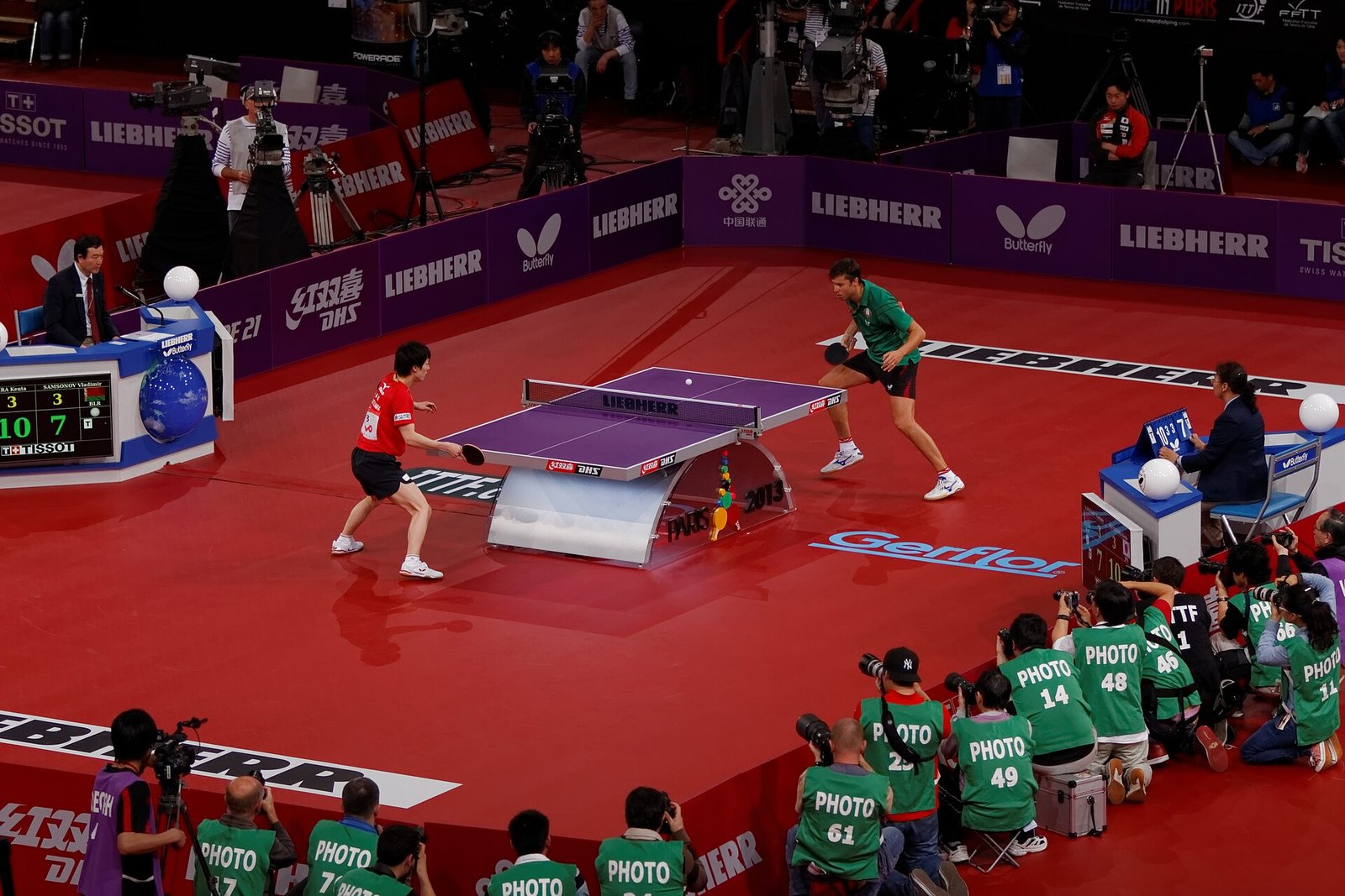 World Championships table tennis match in a full arena, two players rallying on a show court surrounded by photographers