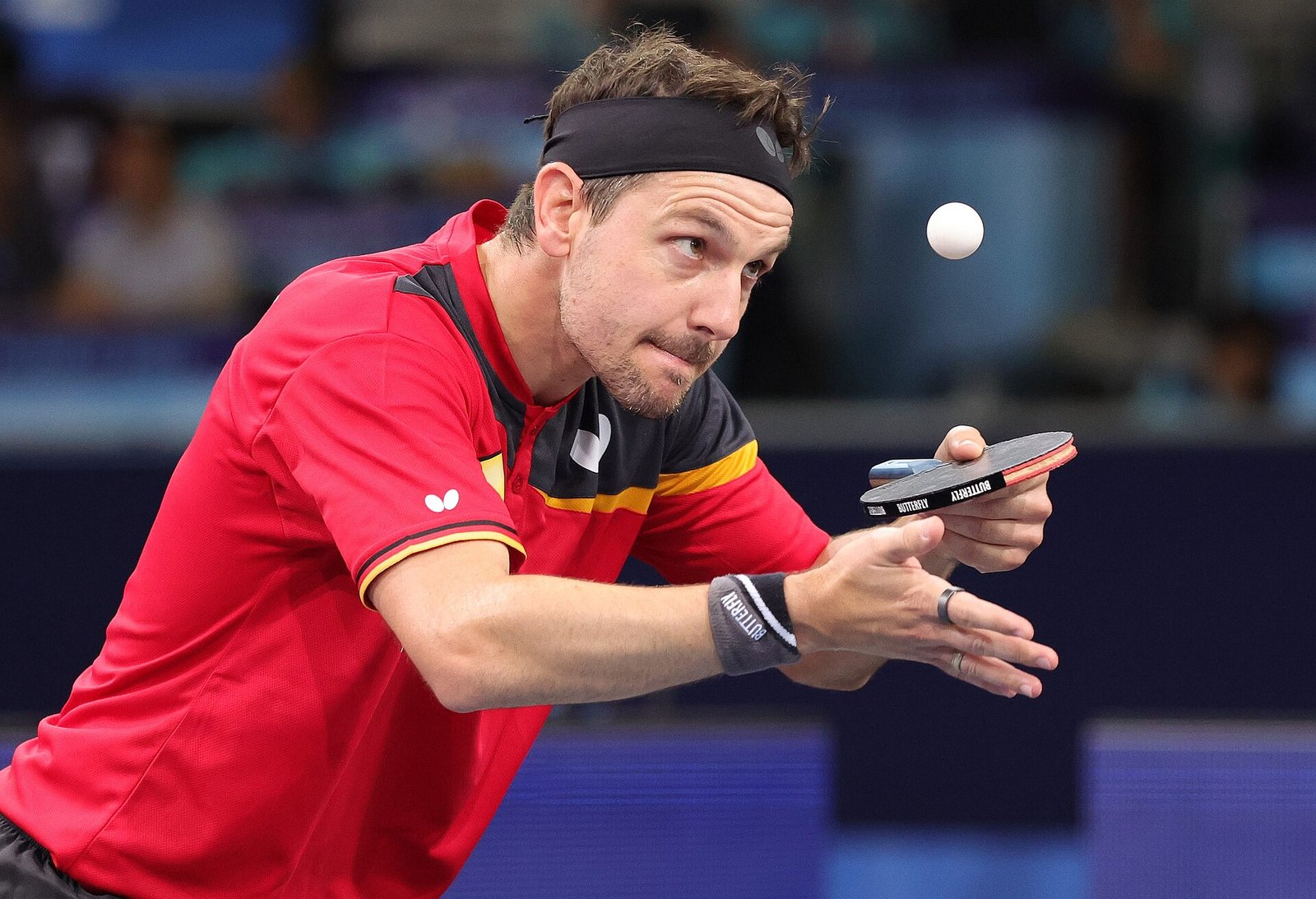 A player a moment after tossing the ball to serve, his free hand open and already moving away from the ball while his racket waits raised beside it