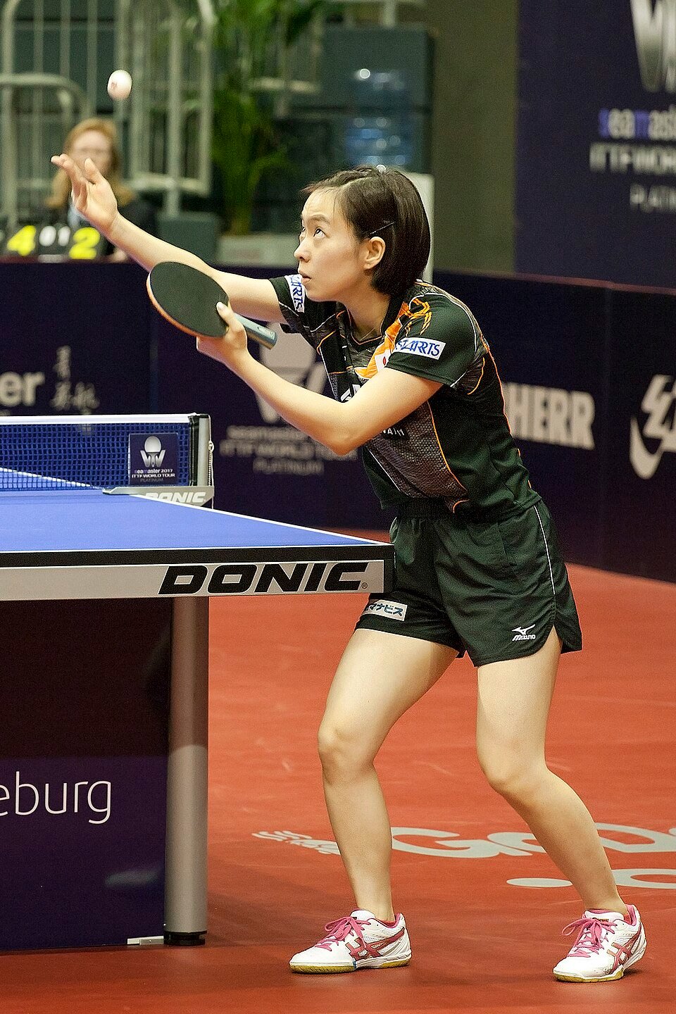 A table tennis player tossing the ball up from an open palm at the start of a legal serve, racket ready behind the end line