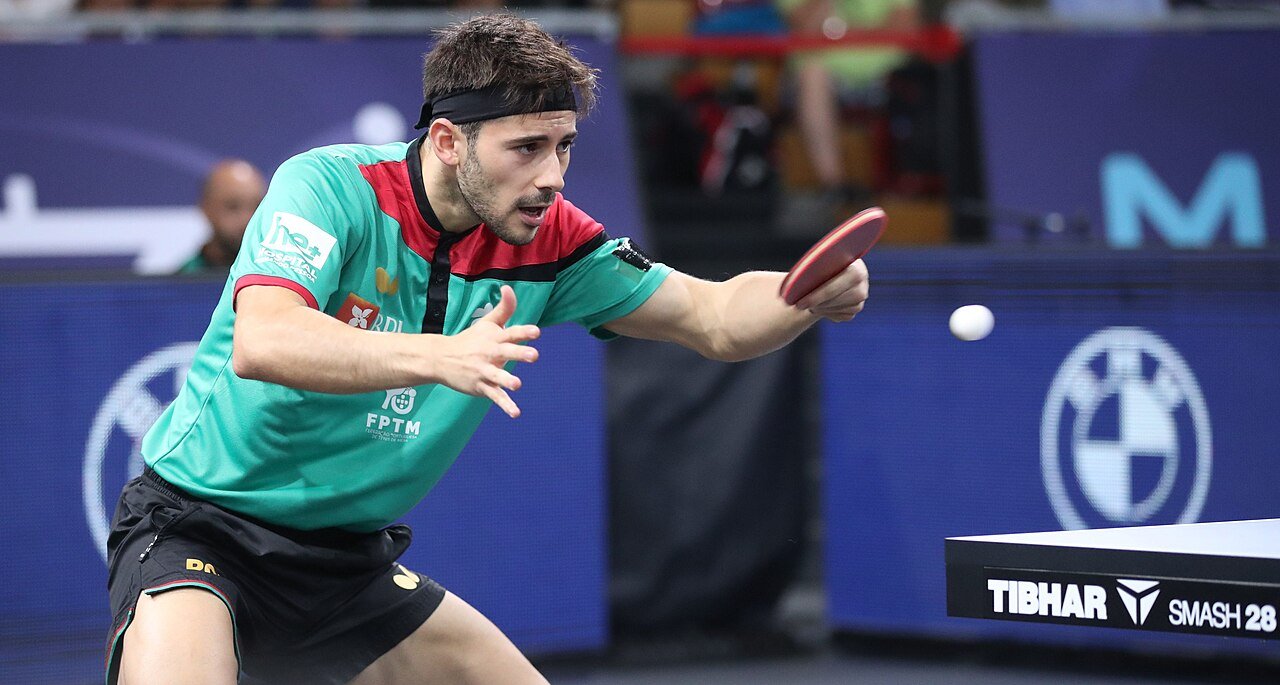 Table tennis player lunging low and wide to his forehand side with his weight shifted onto his right leg and his body opened up to reach a wide ball