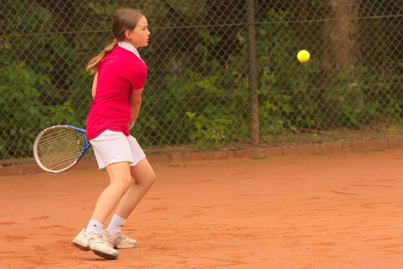 A young player practising groundstrokes on an outdoor tennis court